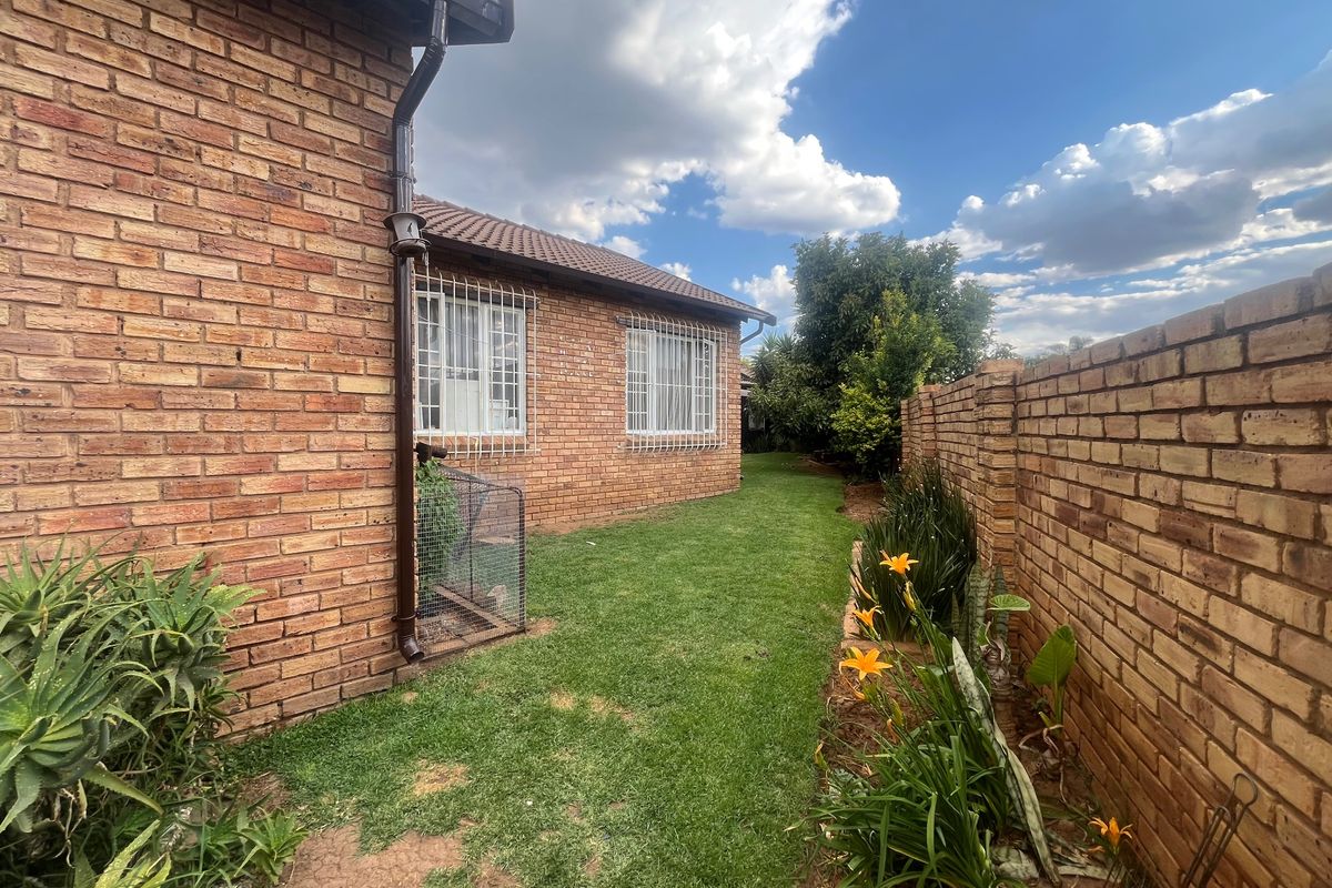 A view of the rear garden featuring a face brick exterior, secure window bars, and a solid brick boundary wall.
