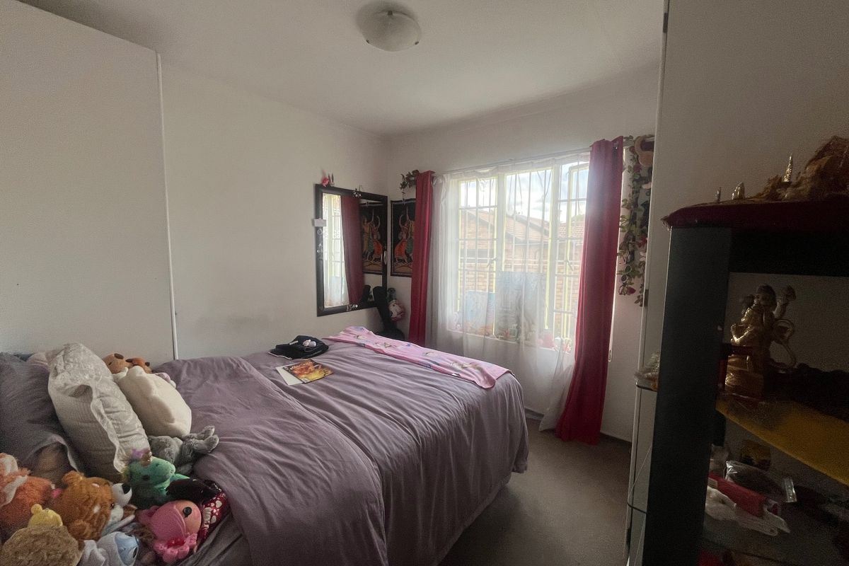 A standard bedroom featuring built-in cupboards and a window with security bars, providing functional space and natural light.