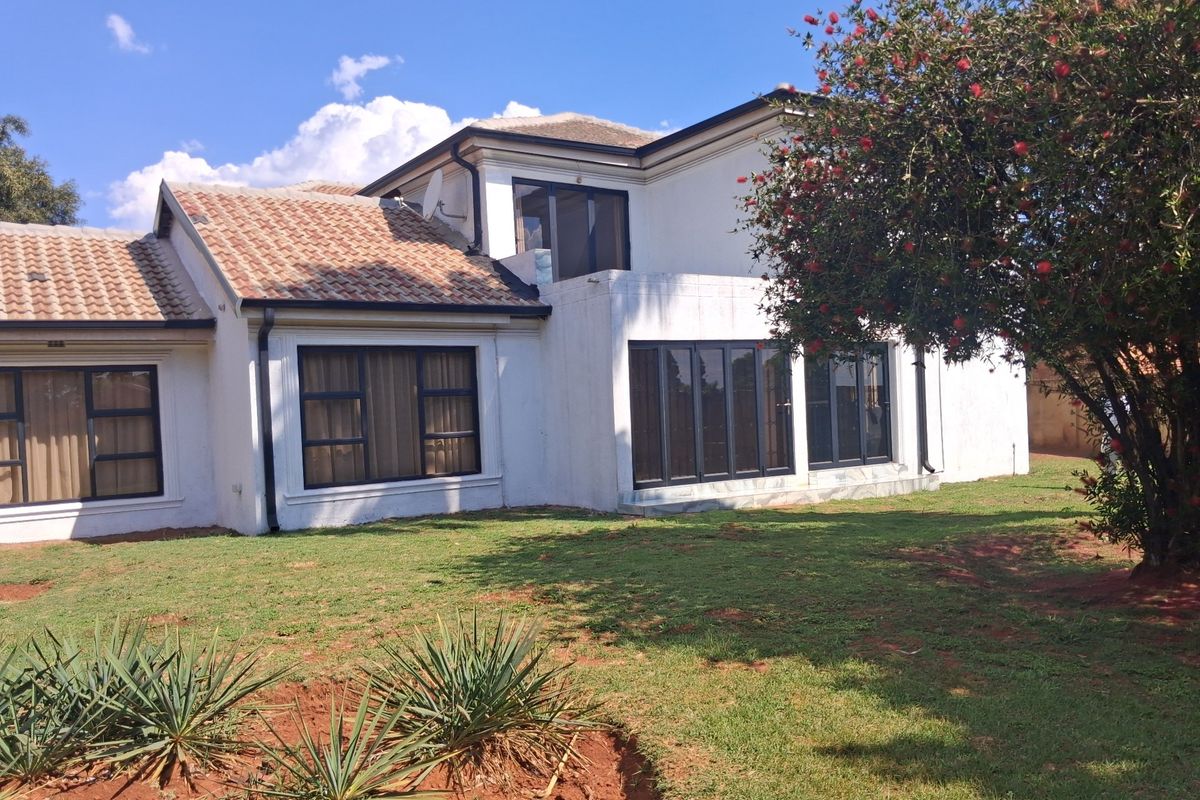 Rear view of a double-story residential property featuring a tiled roof, white exterior walls, and large aluminium-framed windows and sliding doors.