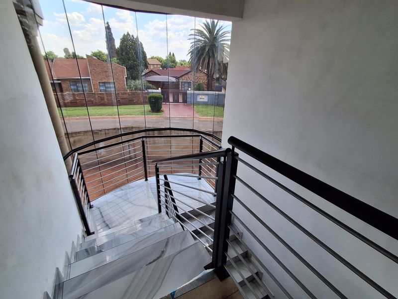 Modern staircase featuring polished marble steps, a sleek metal balustrade, and a curved floor-to-ceiling glass wall offering views of the street.