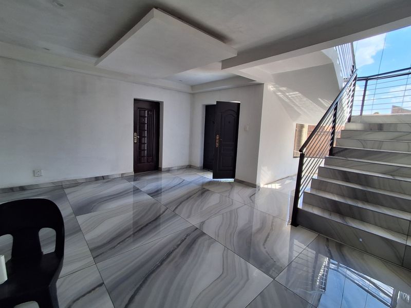 Spacious living area featuring modern large-format marble-look porcelain tiles, a contemporary staircase with metal railings, and a decorative recessed ceiling feature.