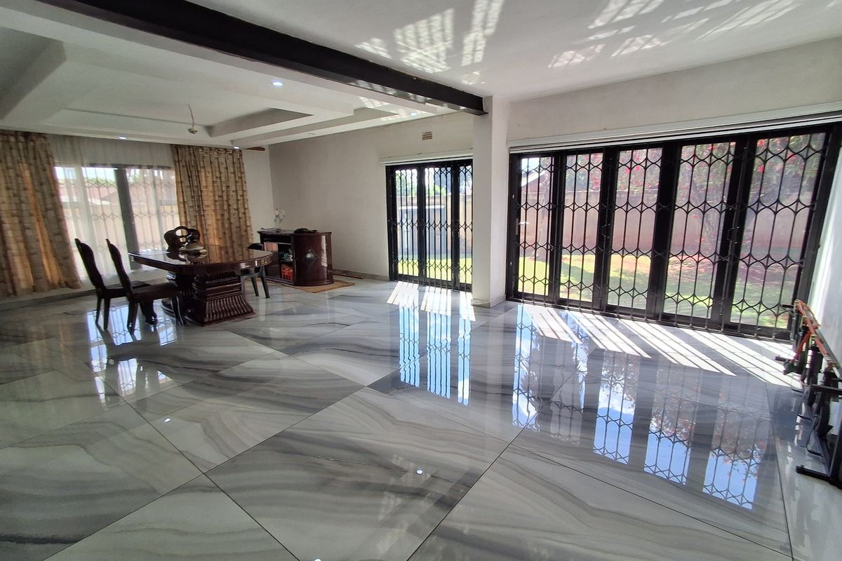 Spacious living area featuring large format marble-look floor tiles, recessed ceiling beams, and expansive black metal folding doors providing seamless access to the garden.