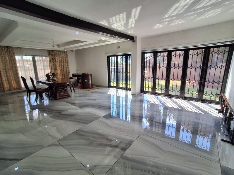 Spacious living area featuring large format marble-look floor tiles, recessed ceiling beams, and expansive black metal folding doors providing seamless access to the garden.