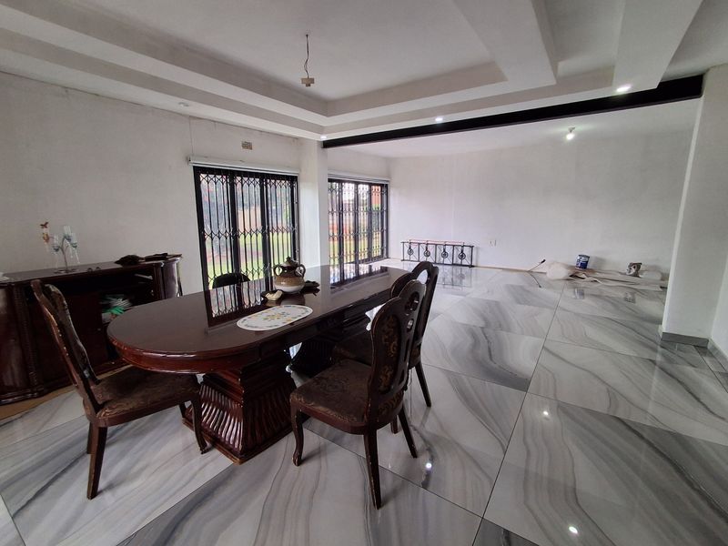 Spacious open-plan living and dining area featuring large-format marble-look floor tiles, recessed tray ceilings, and sliding glass doors with security gates.
