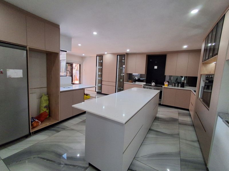 Modern kitchen featuring a large central island, sleek built-in cabinetry, stone countertops, and high-end integrated appliances with polished tiled flooring.