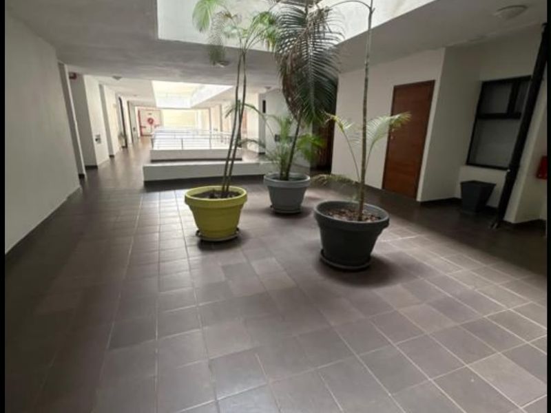 A spacious, well-lit apartment building hallway featuring tiled flooring and a central skylight providing natural illumination.