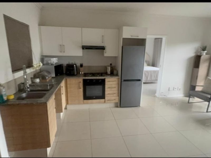 Open-plan kitchen and living area featuring light wood cabinetry, tiled flooring, and direct access to an adjacent bedroom.