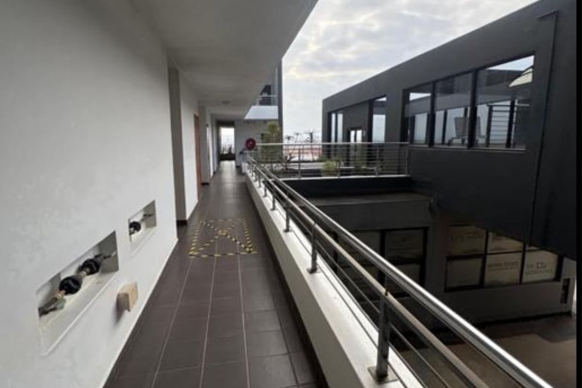 An exterior open-air apartment corridor featuring tiled flooring, a modern stainless steel balustrade, and recessed wall architectural details.