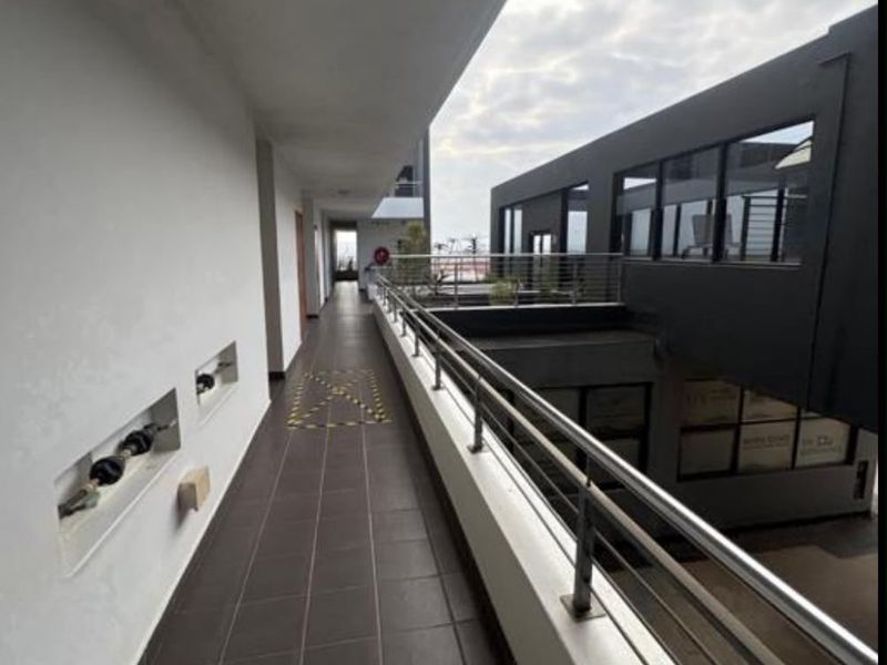 An exterior open-air apartment corridor featuring tiled flooring, a modern stainless steel balustrade, and recessed wall architectural details.