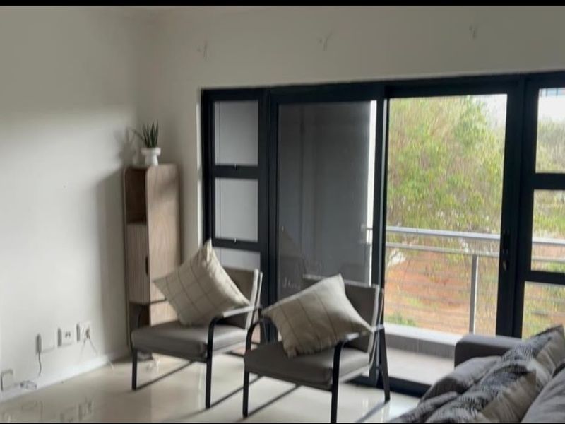 A bright living room featuring large sliding glass doors that open onto a balcony, providing natural light and outdoor access.