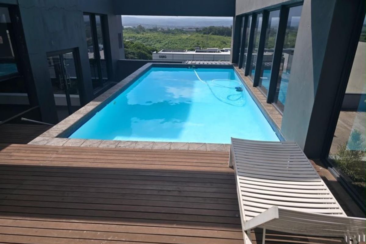 Modern elevated swimming pool area featuring timber decking, recessed lighting, and expansive glass doors offering scenic views.