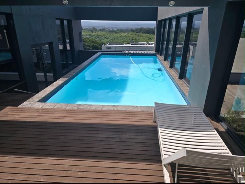 Modern elevated swimming pool area featuring timber decking, recessed lighting, and expansive glass doors offering scenic views.