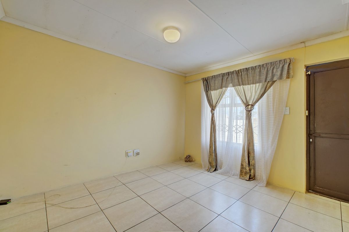 An empty living room featuring tiled flooring, a security gate on the window, and neutral wall finishes, ready for personalization.