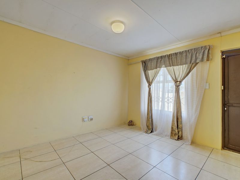 An empty living room featuring tiled flooring, a security gate on the window, and neutral wall finishes, ready for personalization.