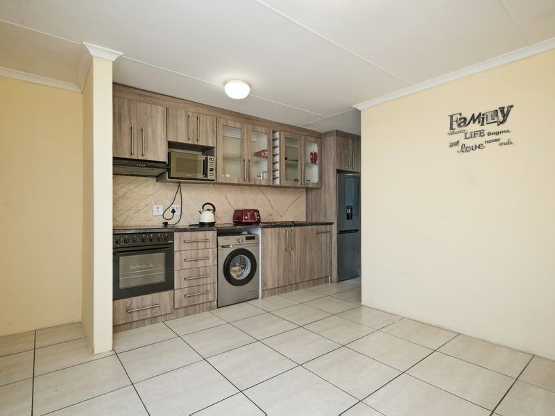 Functional kitchen featuring wood-look cabinetry, tiled flooring, built-in oven with hob, and integrated microwave space, offering a practical layout for daily cooking.