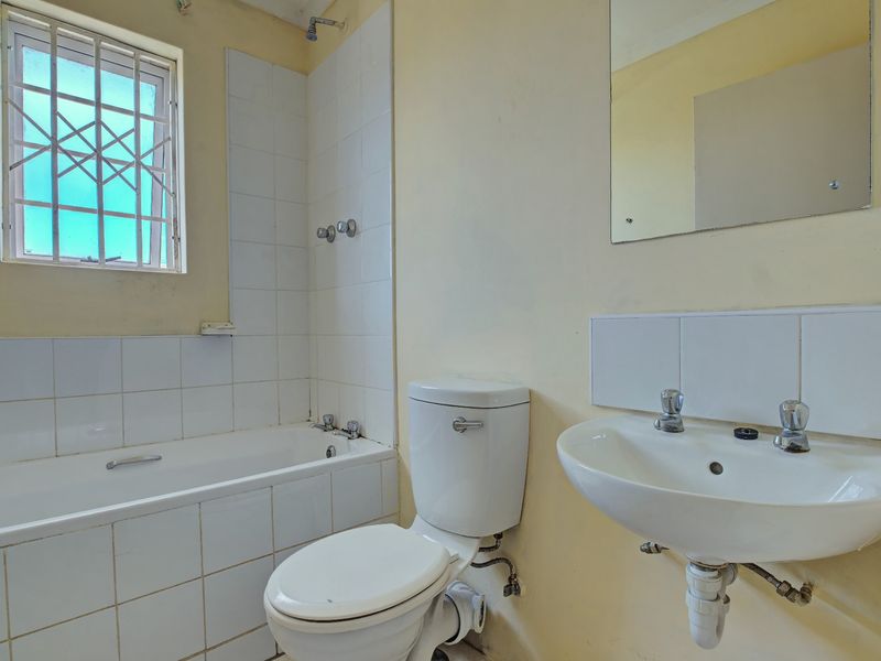 A functional bathroom featuring a bathtub with shower mixer, pedestal basin, and toilet, requiring cosmetic updates to improve its overall aesthetic appeal.
