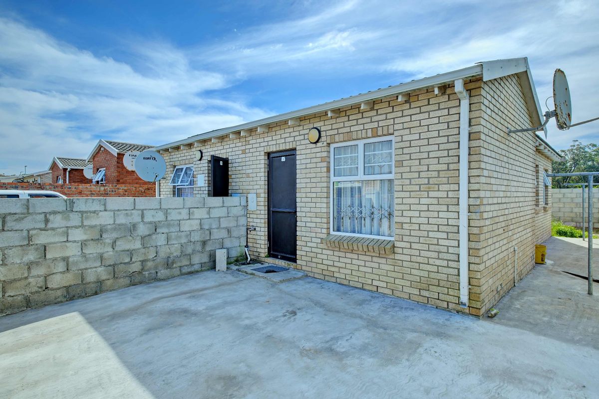 Rear exterior view of a face brick house featuring a concrete patio, security gate, and window security bars.