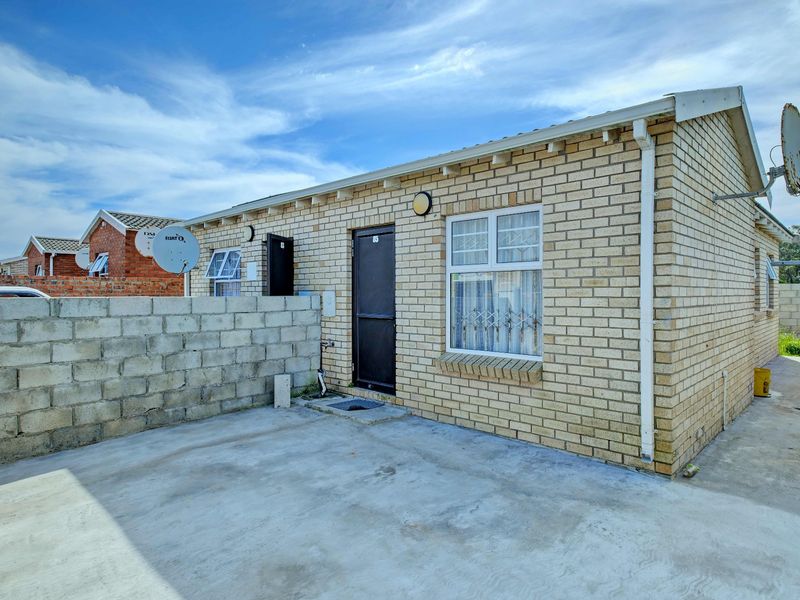 Rear exterior view of a face brick house featuring a concrete patio, security gate, and window security bars.