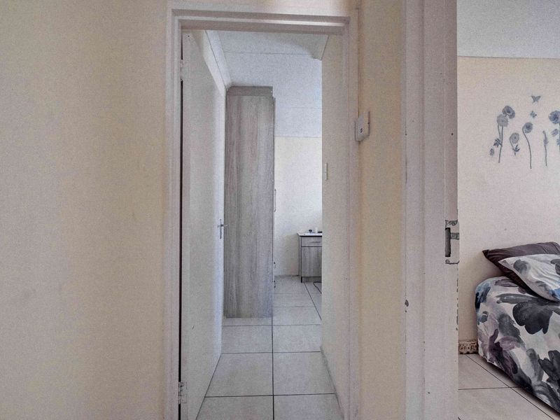 A functional hallway featuring tiled flooring and a built-in cupboard, providing access to adjacent rooms within the home.