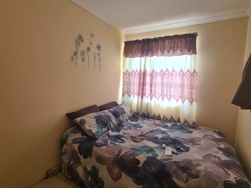 A compact bedroom featuring tiled flooring and a window, currently requiring cosmetic updates to the wall finishes.