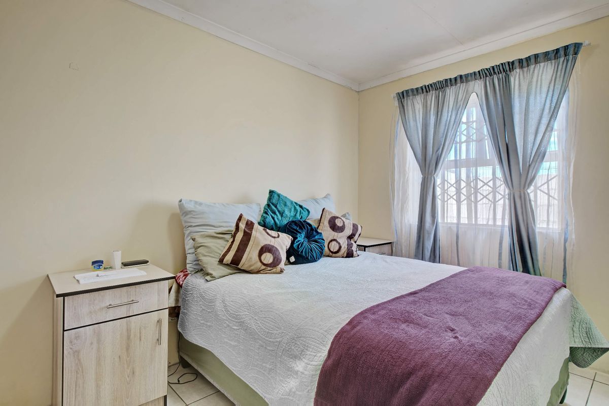 A functional bedroom featuring tiled flooring, a window with a security gate, and neutral wall finishes.