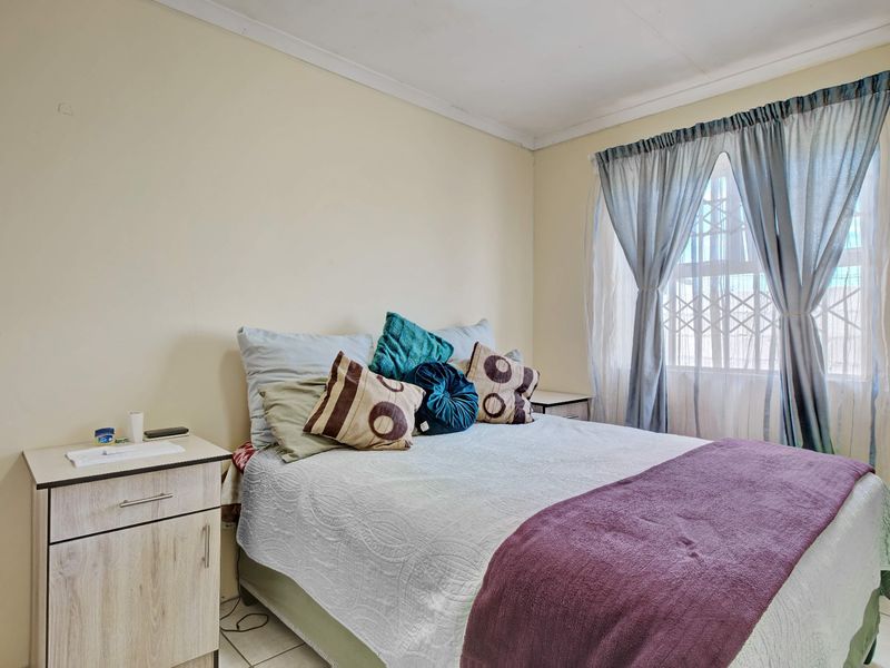 A functional bedroom featuring tiled flooring, a window with a security gate, and neutral wall finishes.