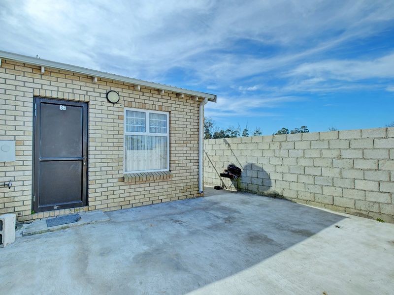 Rear exterior view of the property featuring a brick facade, a concrete patio area, and a cinder block boundary wall.