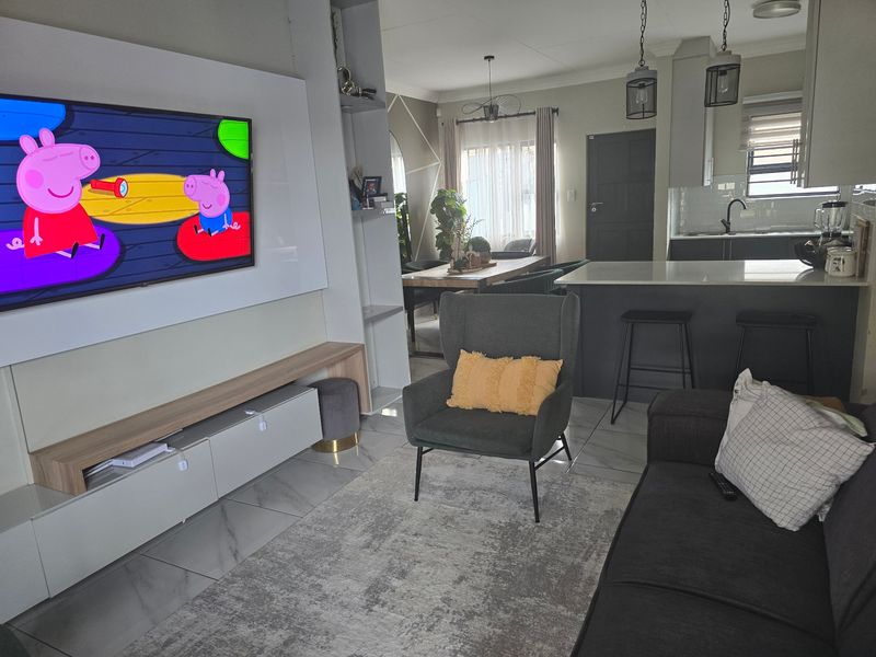 Modern open-plan living area featuring a sleek kitchen island, built-in media cabinetry, and contemporary tiled flooring, creating a cohesive and functional living space.
