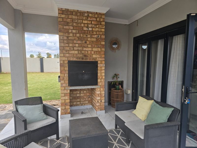 Covered patio area featuring a built-in brick fireplace, tiled flooring, and direct access to the garden through sliding glass doors.