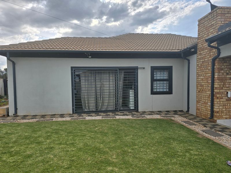 Rear view of the house featuring a tiled roof, brick chimney, sliding glass door with security gate, and a well-maintained lawn with paved walkway.