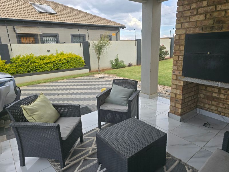Covered patio area featuring a built-in brick braai, polished tile flooring, and direct access to a paved courtyard and landscaped garden.