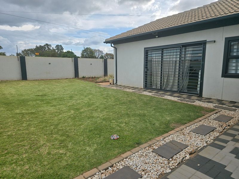 A well-maintained rear garden featuring a manicured lawn, paved pathways, and a secure perimeter wall with electric fencing.