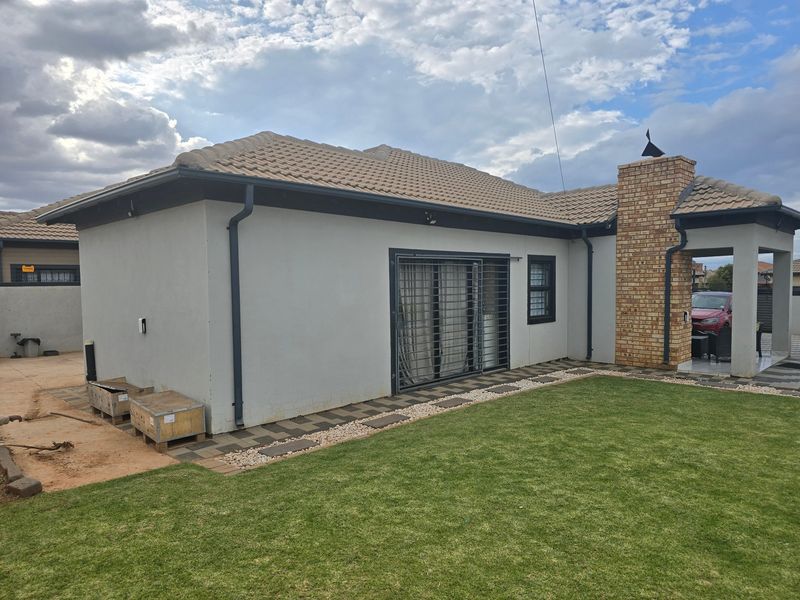 Rear view of the property featuring a tiled roof, brick chimney, and a paved walkway leading to a sliding door with security gate.