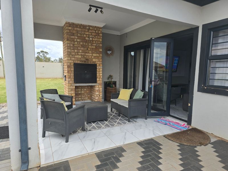 Covered patio area featuring a built-in brick braai, modern tiled flooring, and aluminium stack doors providing seamless access to the interior living space.
