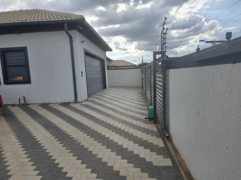 A well-maintained paved driveway leading to a garage, featuring a secure perimeter wall with electric fencing and a sliding gate.