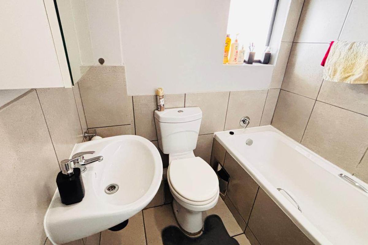 A functional bathroom featuring neutral ceramic wall and floor tiles, a pedestal washbasin, a close-coupled toilet, and a built-in bathtub.