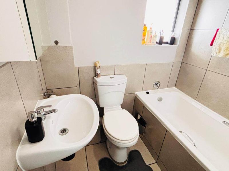 A functional bathroom featuring neutral ceramic wall and floor tiles, a pedestal washbasin, a close-coupled toilet, and a built-in bathtub.