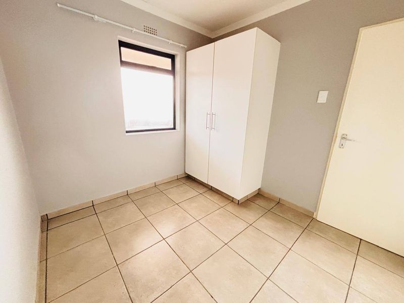 A clean, empty bedroom featuring neutral tiled flooring, a built-in wardrobe, and a window providing natural light.