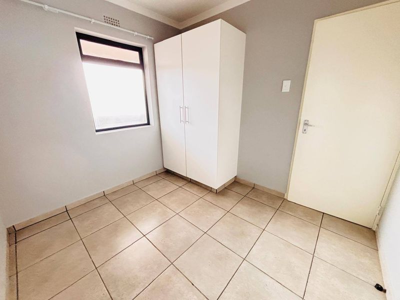 A clean, neutral bedroom featuring tiled flooring, a built-in wardrobe, and natural light from the window.