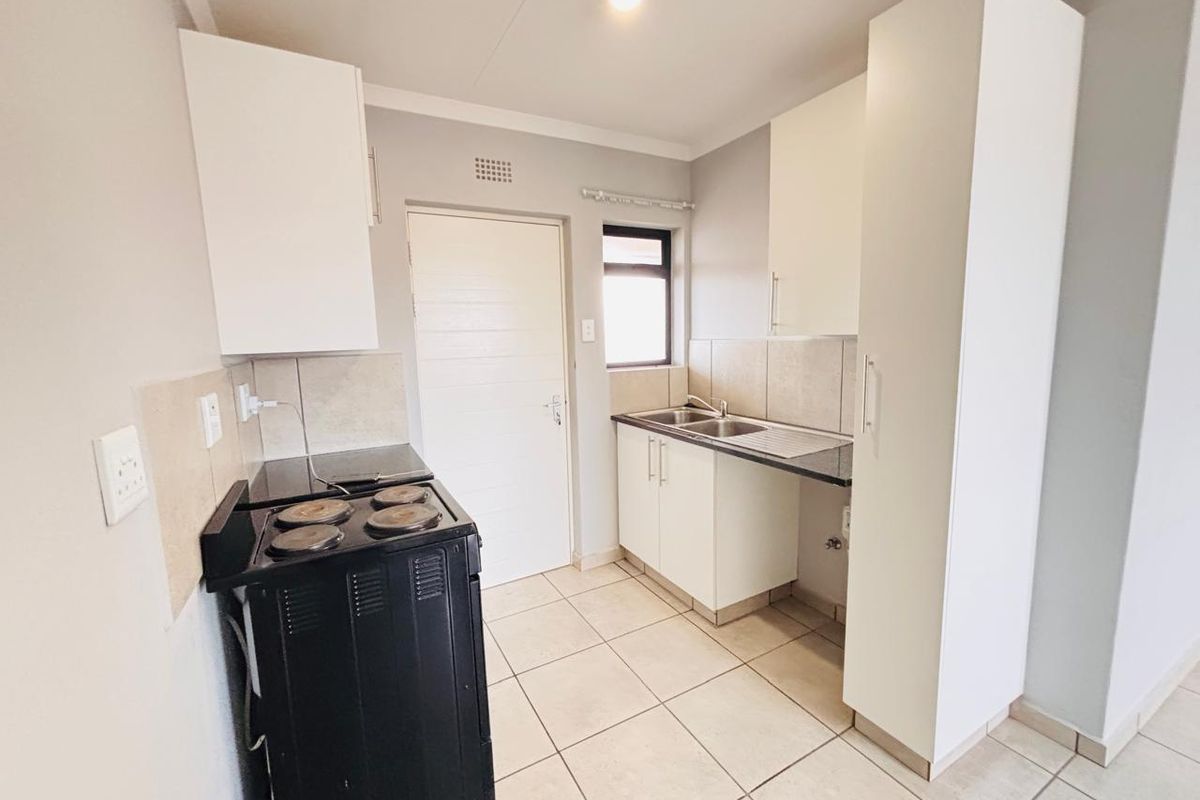 A functional kitchen featuring white built-in cabinetry, a double sink, tiled backsplash, and tiled flooring, providing a clean and practical workspace.