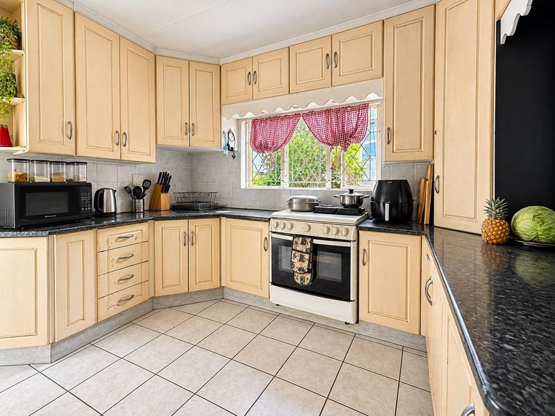 A functional kitchen featuring light-toned built-in cabinetry, dark granite countertops, tiled flooring, and a freestanding oven with a tiled backsplash.