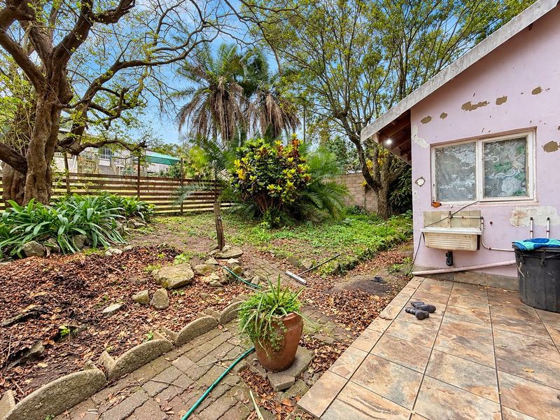 Rear garden area featuring a tiled patio, external utility sink, and mature landscaping, requiring exterior maintenance and painting to improve curb appeal.