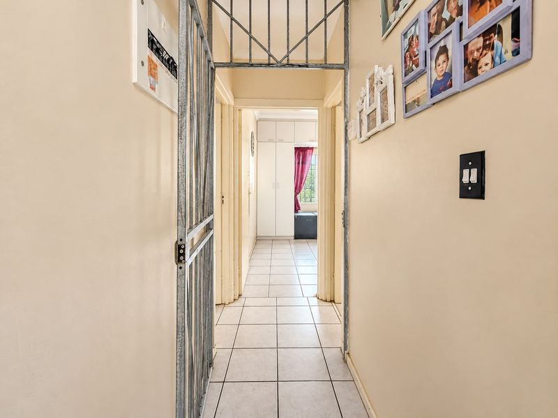 A functional hallway featuring tiled flooring, a security gate, and access to built-in storage cupboards.