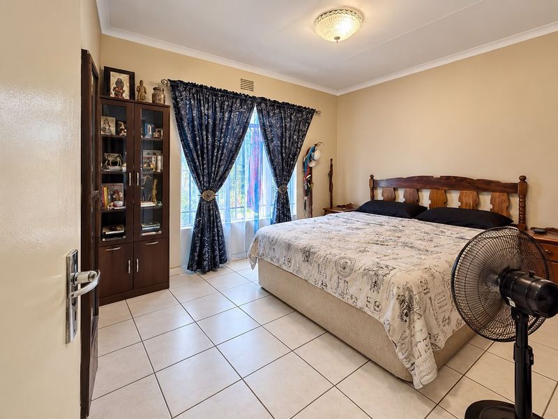 A well-lit bedroom featuring neutral wall tones, tiled flooring, and a large window, offering a comfortable and functional living space.
