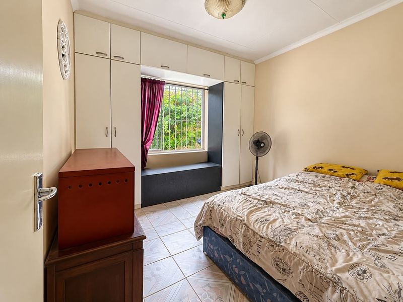 A bedroom featuring built-in cupboards, tiled flooring, and a window with security bars, offering a functional space with potential for modern updates.
