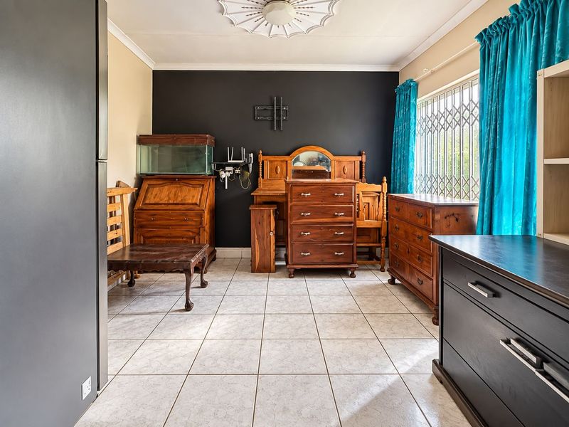 A bedroom featuring ceramic floor tiles, a decorative ceiling rose, and a window fitted with a security gate.