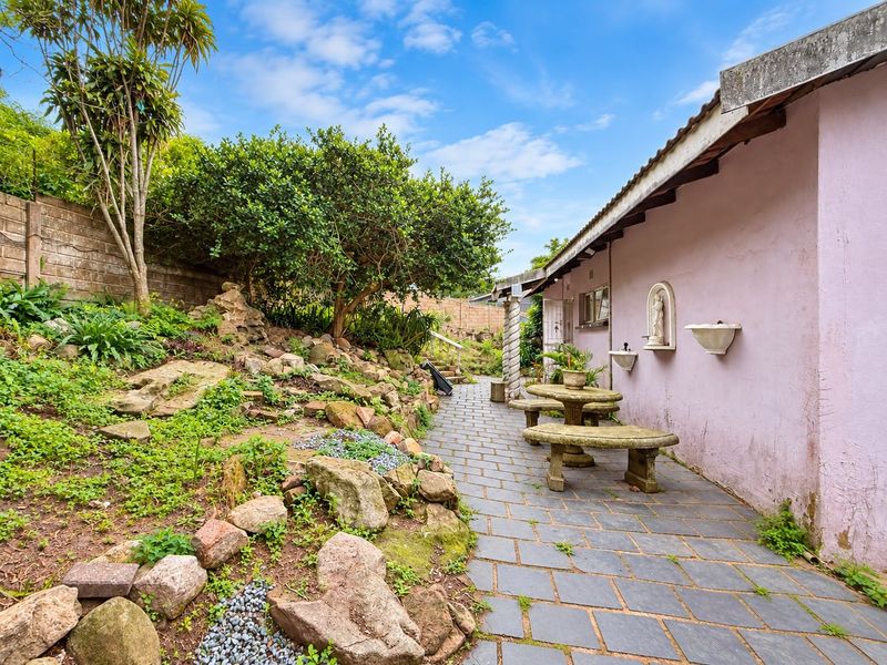 A rear exterior view featuring a paved patio area, stone-landscaped garden beds, and a building facade with decorative wall-mounted features.