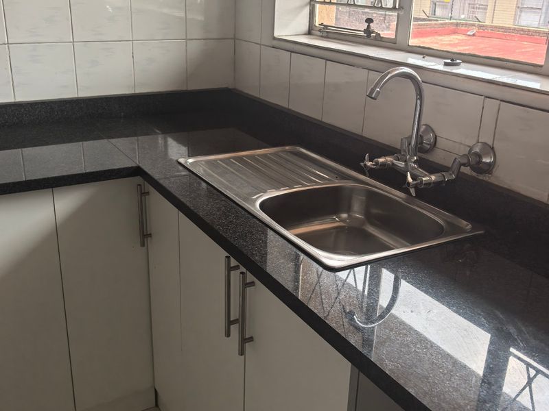 A functional kitchen area featuring granite countertops, a stainless steel sink with mixer tap, and white cabinetry with tiled backsplash.