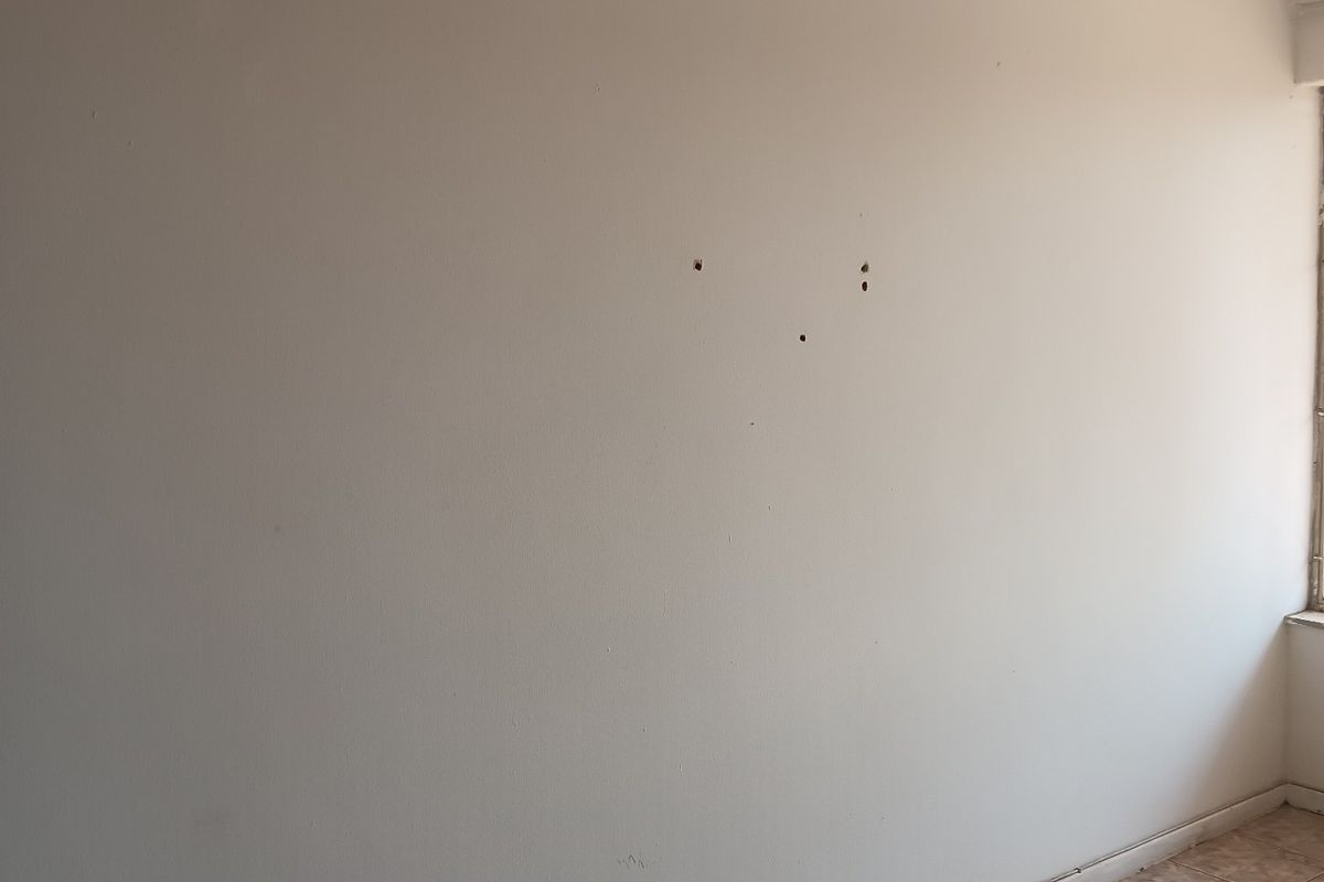 An empty bedroom featuring tiled flooring and a textured ceiling, currently showing minor wall surface damage.