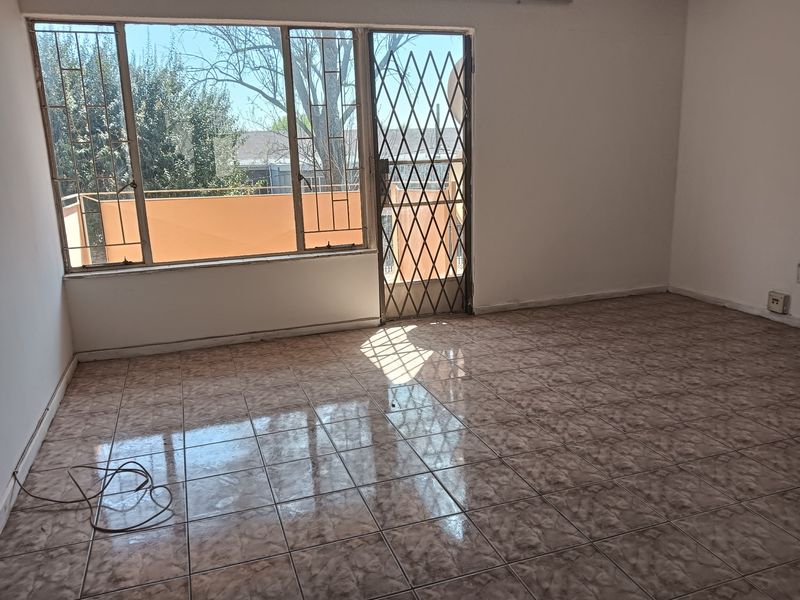 An empty living room featuring tiled flooring, a large window, and a security gate leading to an outdoor area.